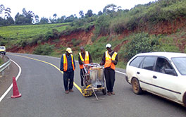 Workers using a hand-push thermoplastic road marking machine on a highway